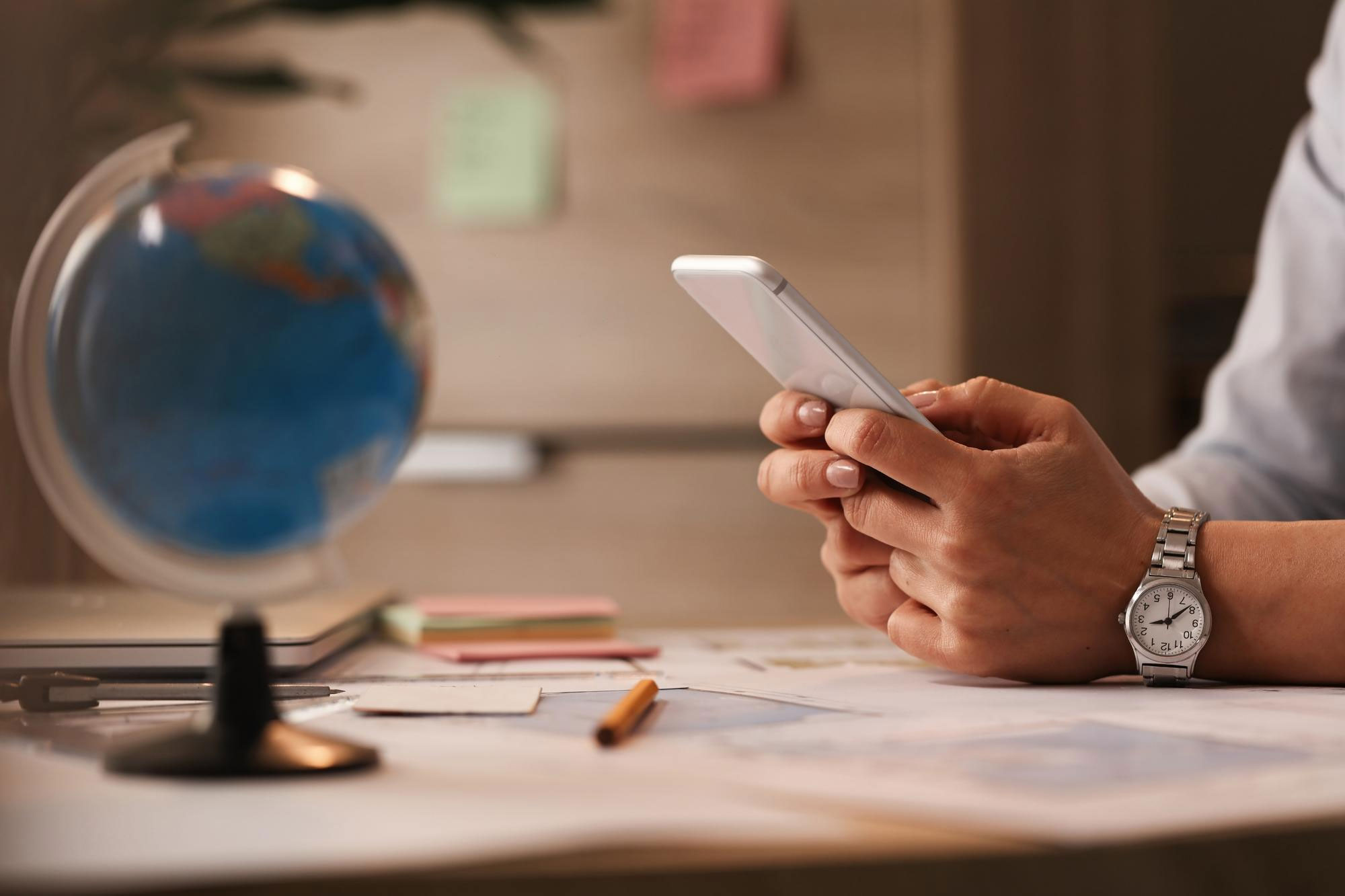 Hands holding a smartphone at a desk with a globe, representing localization for global audiences